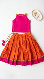 A two-piece children's traditional outfit laid flat on a white background, featuring a sleeveless bright pink top with gold trim and a matching pleated orange skirt with gold polka dots and a pink border.